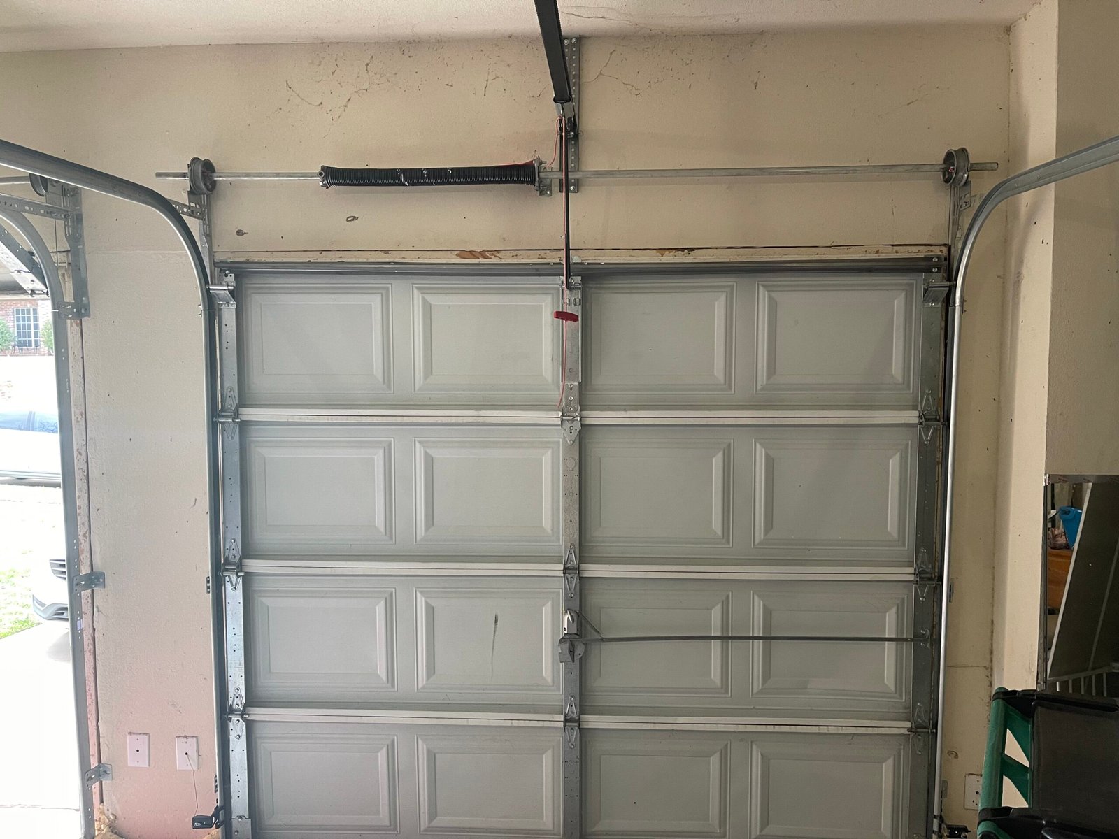 Extension spring, cable and opener rail above a white raised-panel garage door
